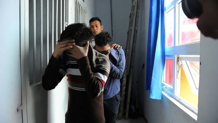 A police officer escorts two men accused of having gay sex into a holding cell prior to their trial at sharia court in Banda Aceh AP